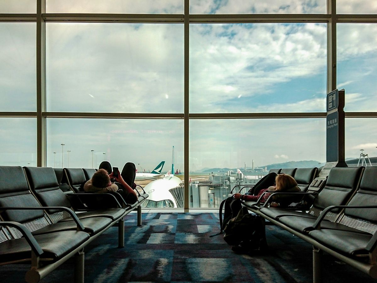 Travelers lying across airport terminal seating to sleep