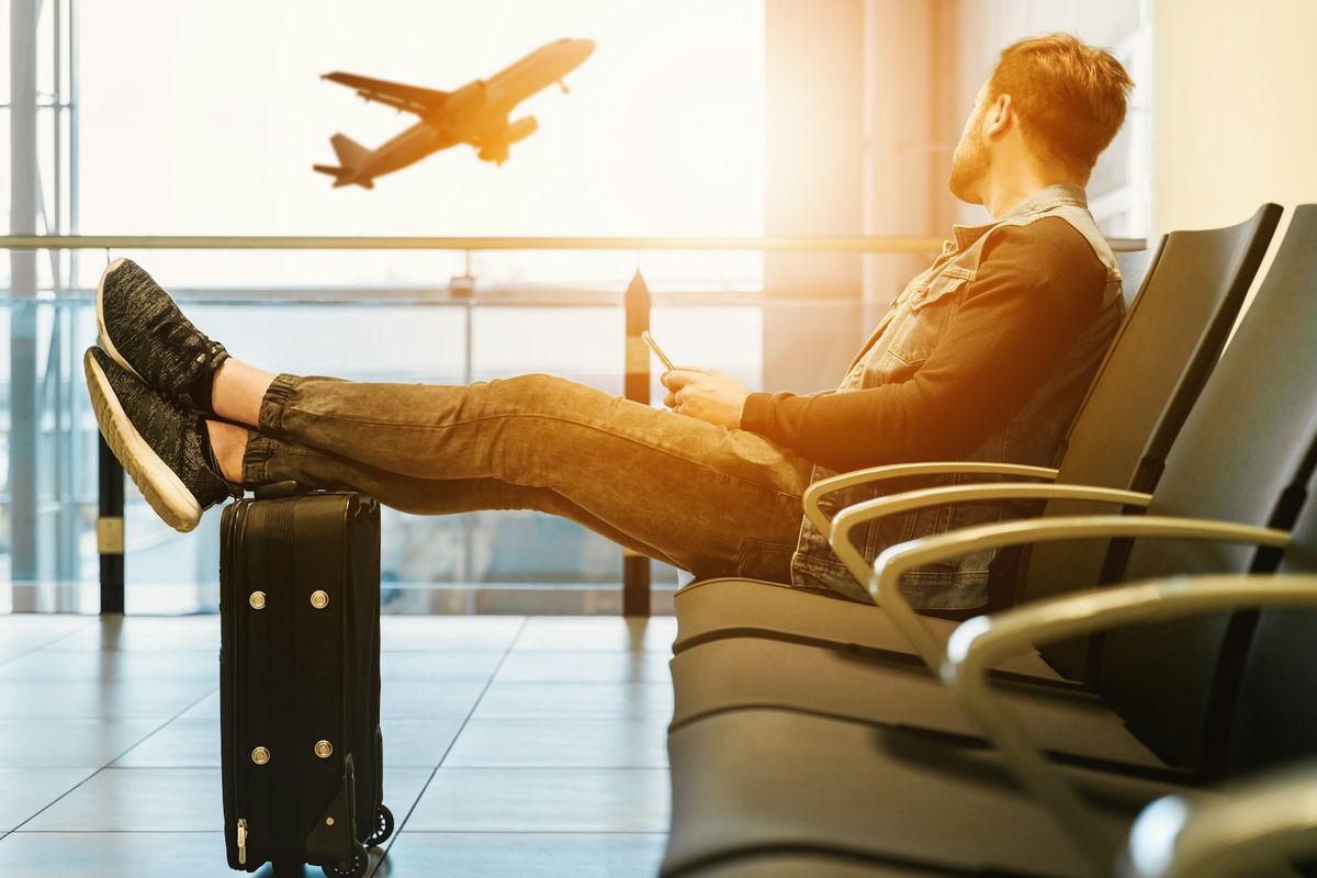 Traveller sitting with feet on luggage watching planes at airport