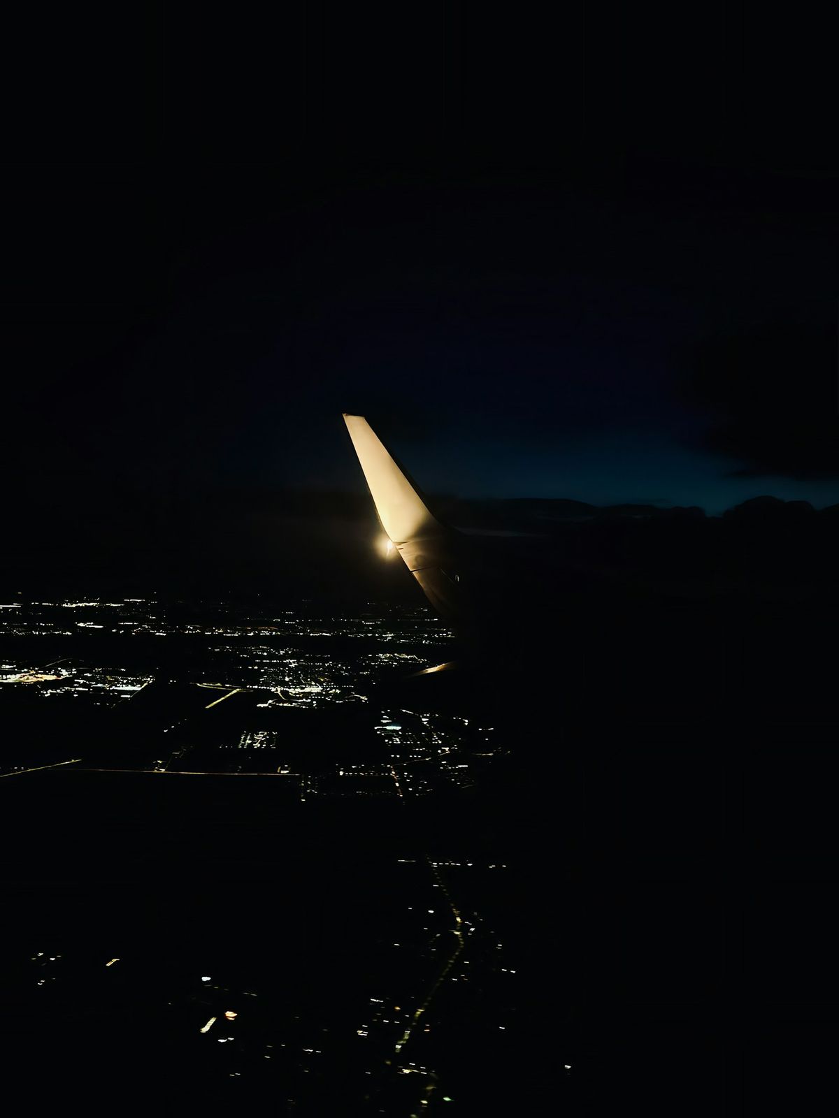 Airplane wing over city lights seen from a window at night