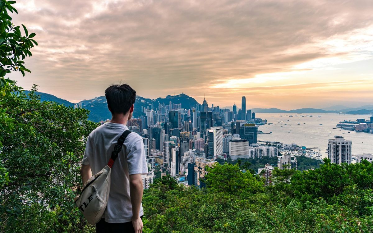 A traveller with a backpack overlooking a city skyline from a hillside