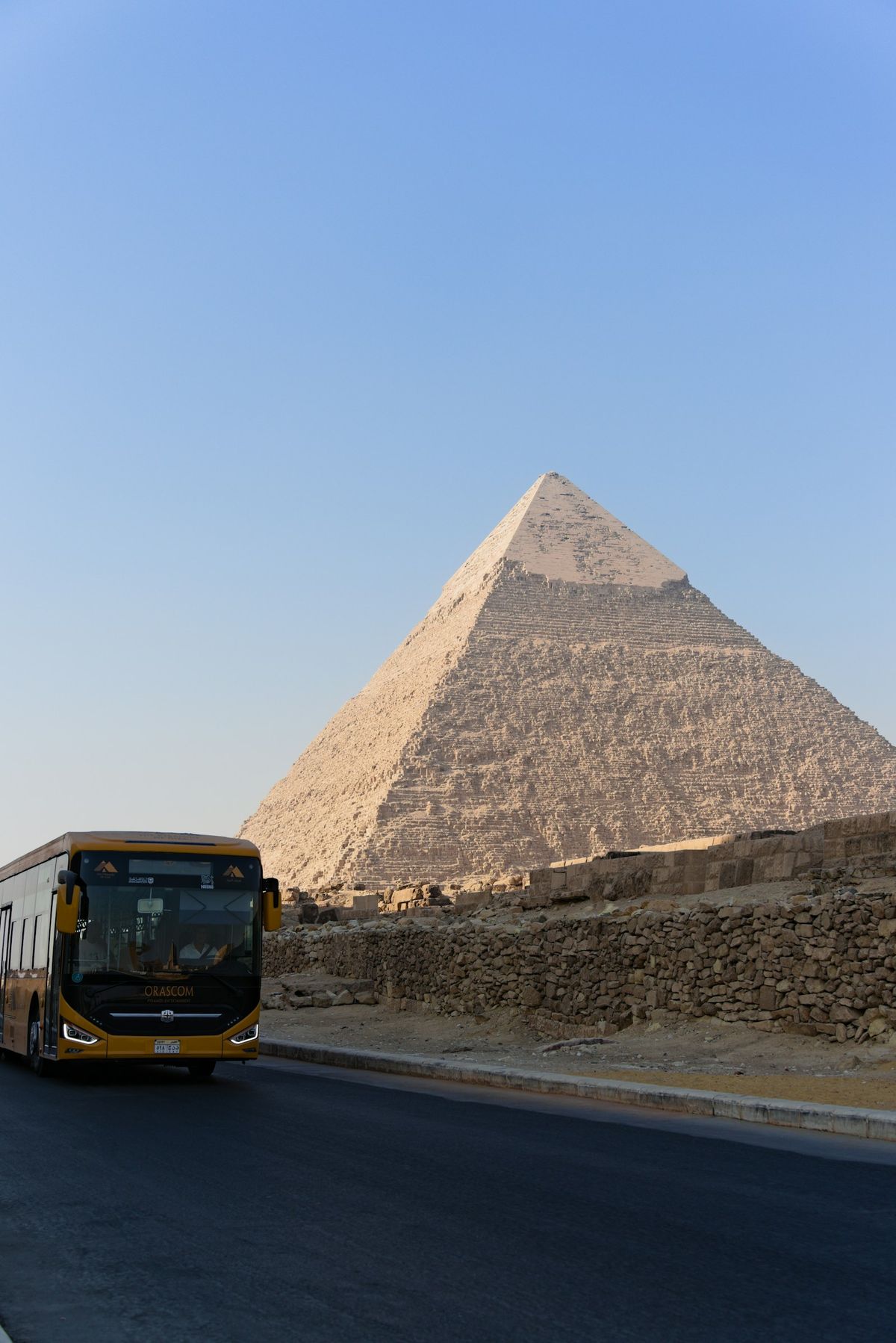 Yellow long-distance bus driving past a pyramid in the Egyptian desert