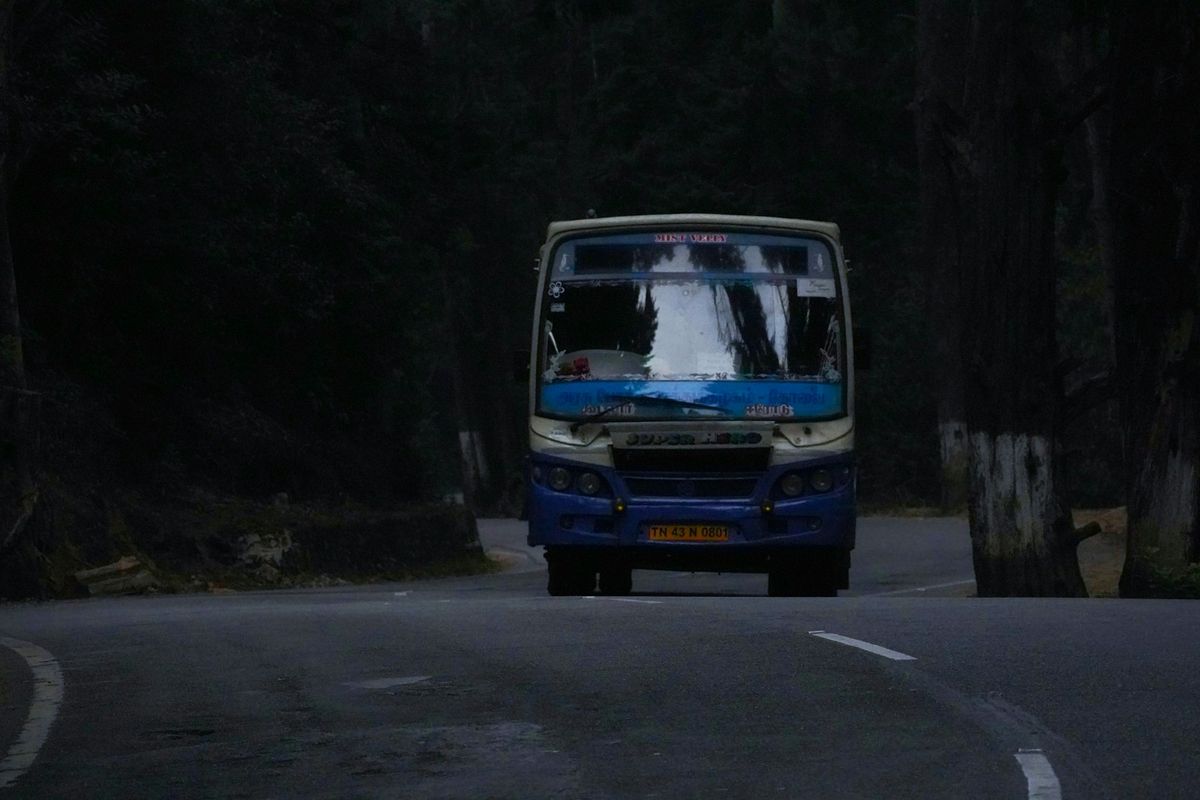 Blue and white bus driving down an Indian road