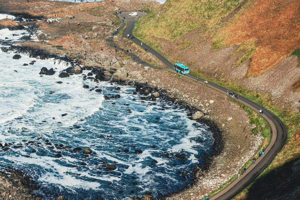 Turquoise bus driving along a scenic coastal road in Ireland