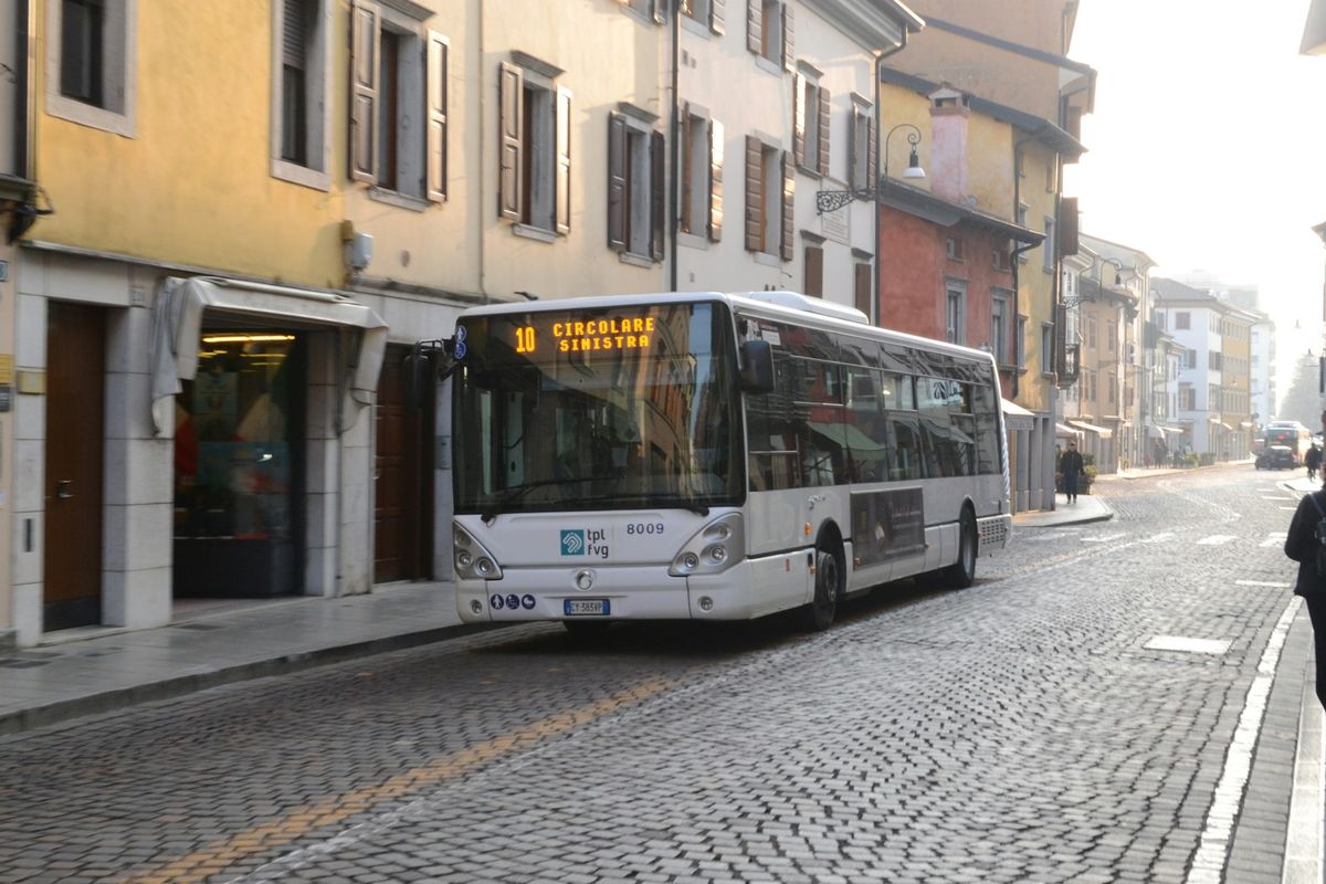 White coach bus driving down a cobblestone street in Italy
