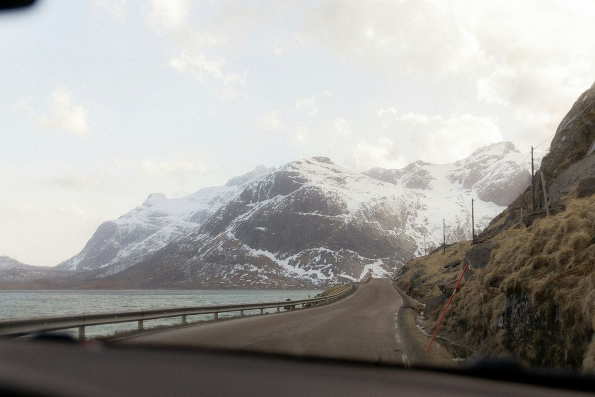 Road stretches towards snowy mountains and sea in Scandinavia