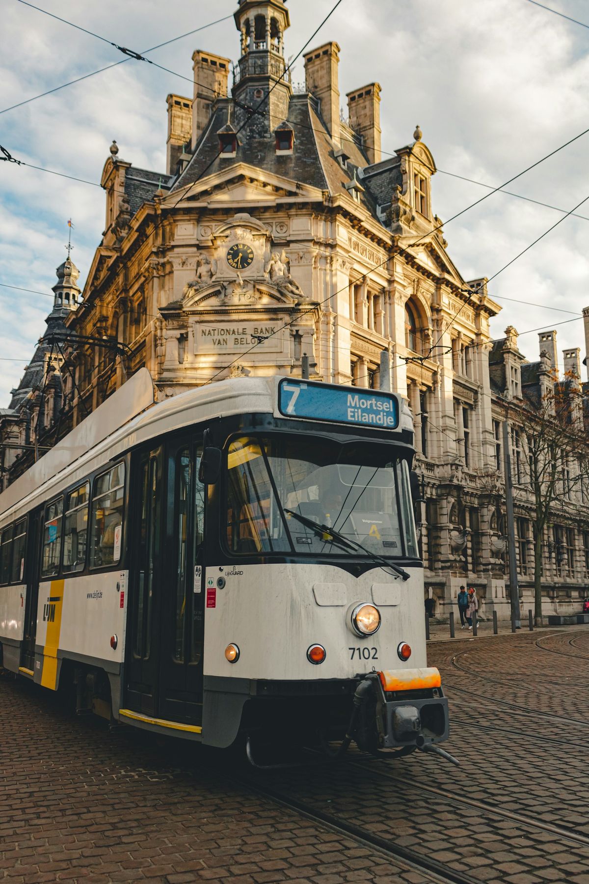 White and yellow tram in front of a brown concrete building in Antwerp