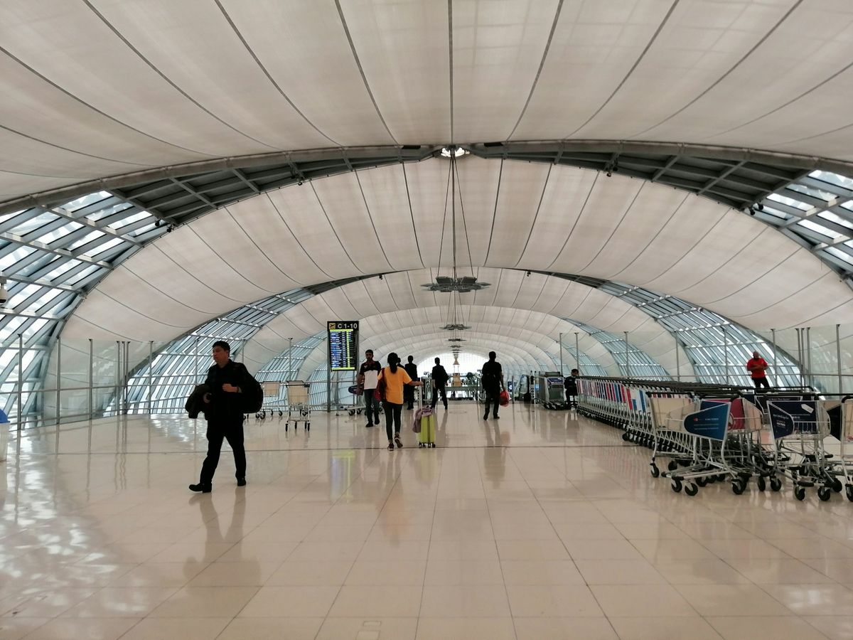 Travelers walking inside Suvarnabhumi Airport's white terminal building, Bangkok