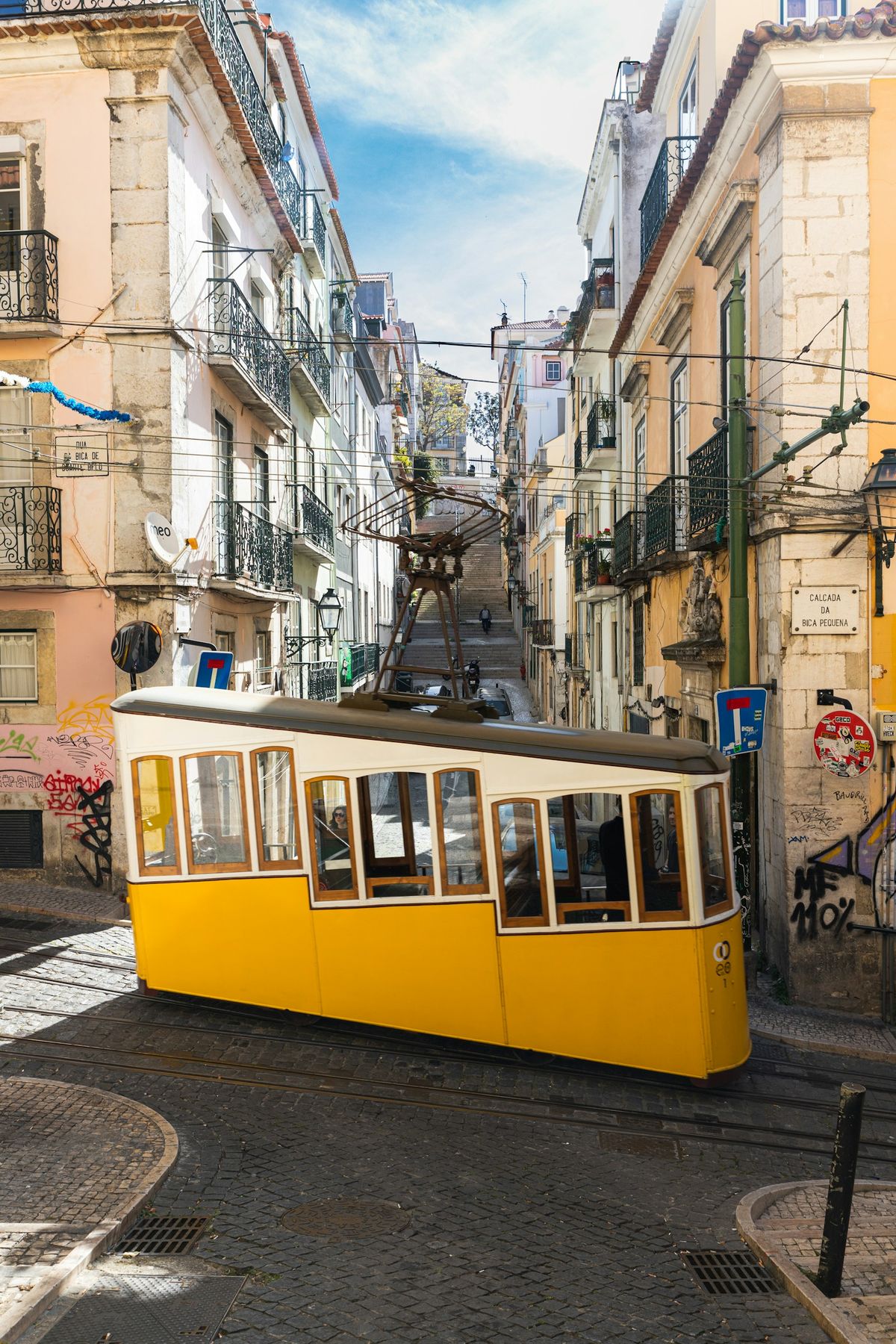 Yellow Elevador da Bica funicular tram climbing a steep narrow street in Lisbon