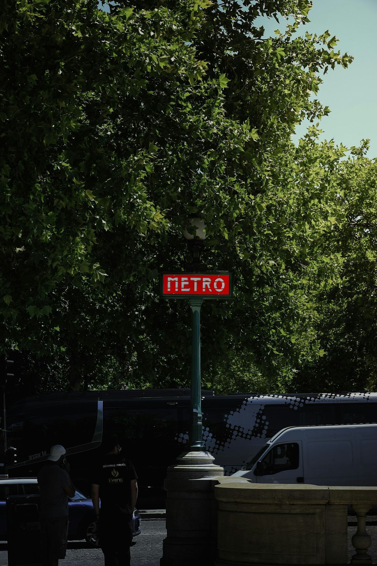 Red Paris Metro sign beneath green trees