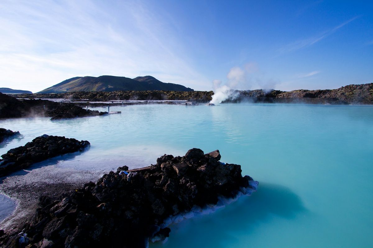 Calm geothermal water beside mountains under blue sky in Iceland