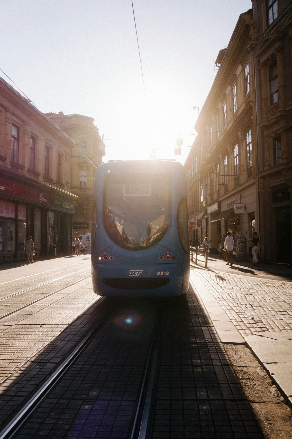 Blue tram travelling down a sunlit city street in Zagreb
