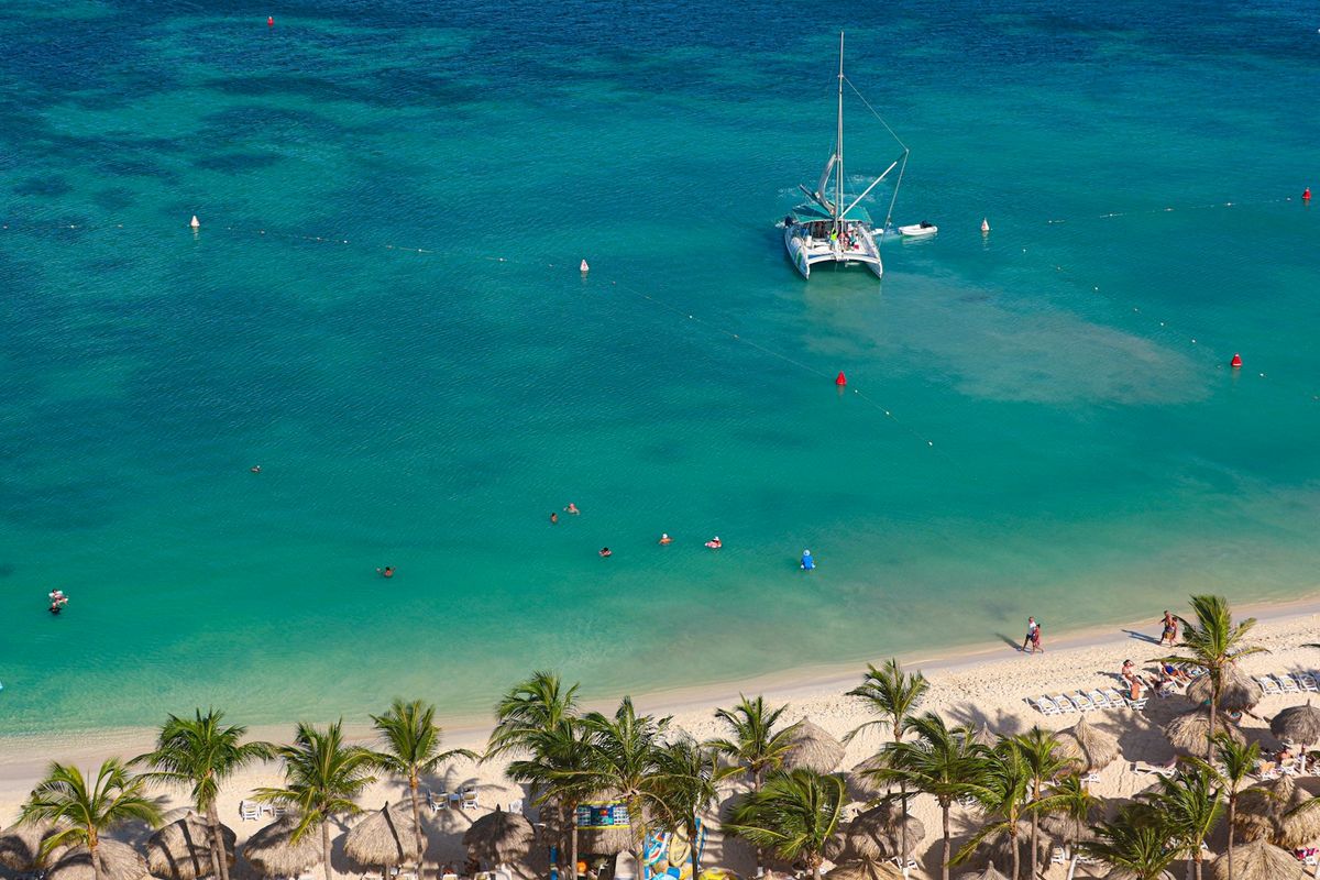 Catamaran sailing through clear turquoise ocean near a Caribbean beach