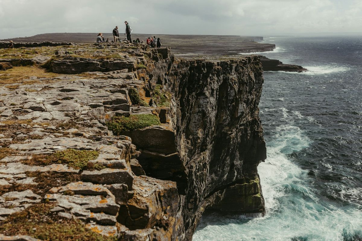 Visitors standing on the limestone cliff edge of Inishmore, Aran Islands