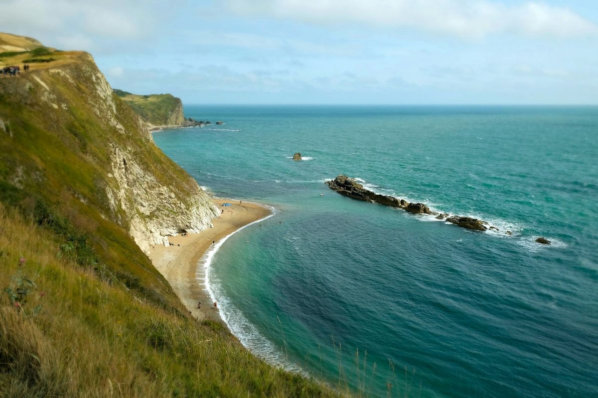 Green cliffs meeting turquoise ocean with a small beach in southwest England