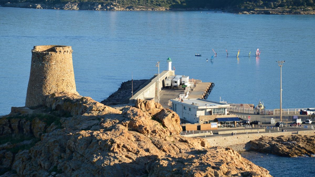 Old stone tower on rocky Corsica coast with harbor