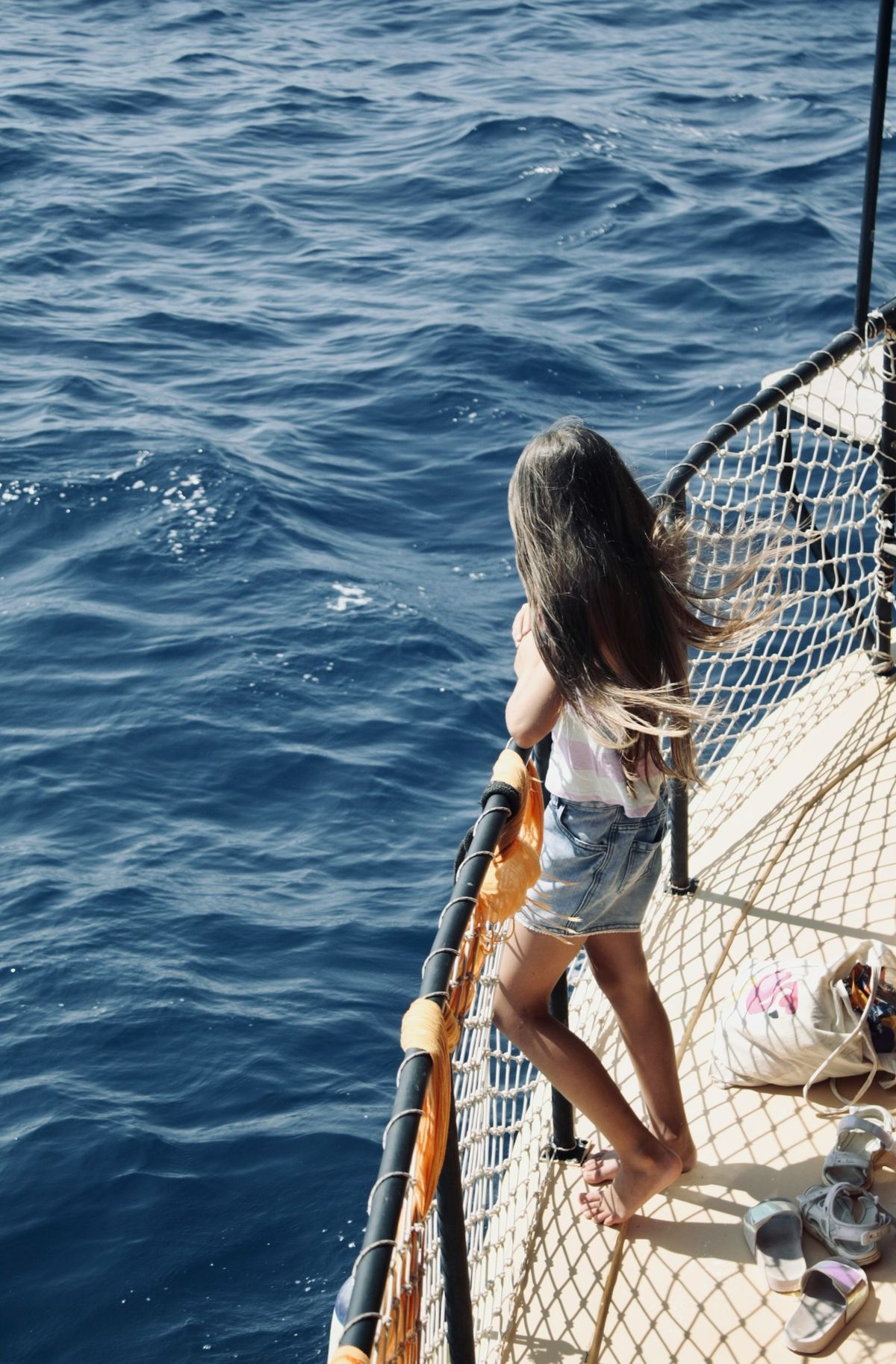 A little girl standing on the deck of a ferry looking out to sea