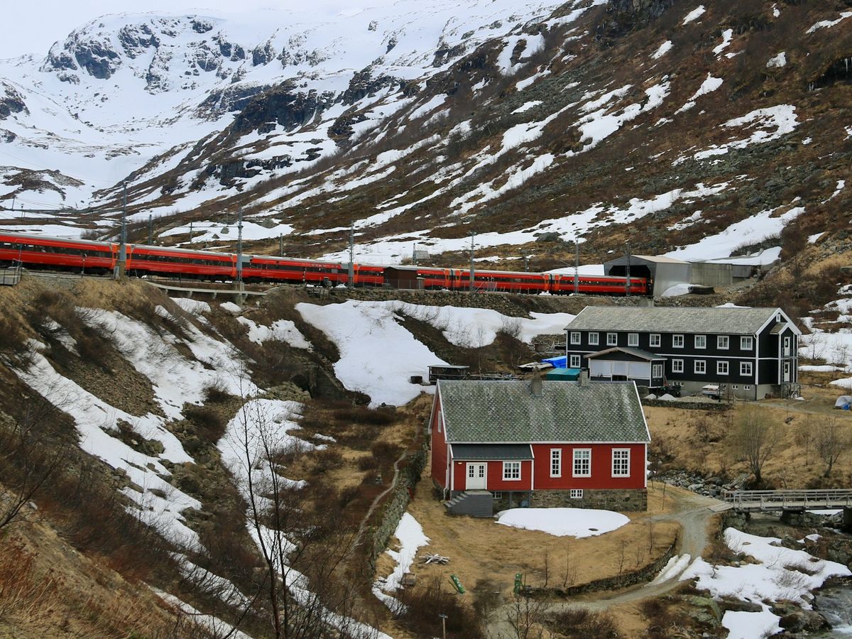 Red train traveling through snowy Norwegian mountain landscape