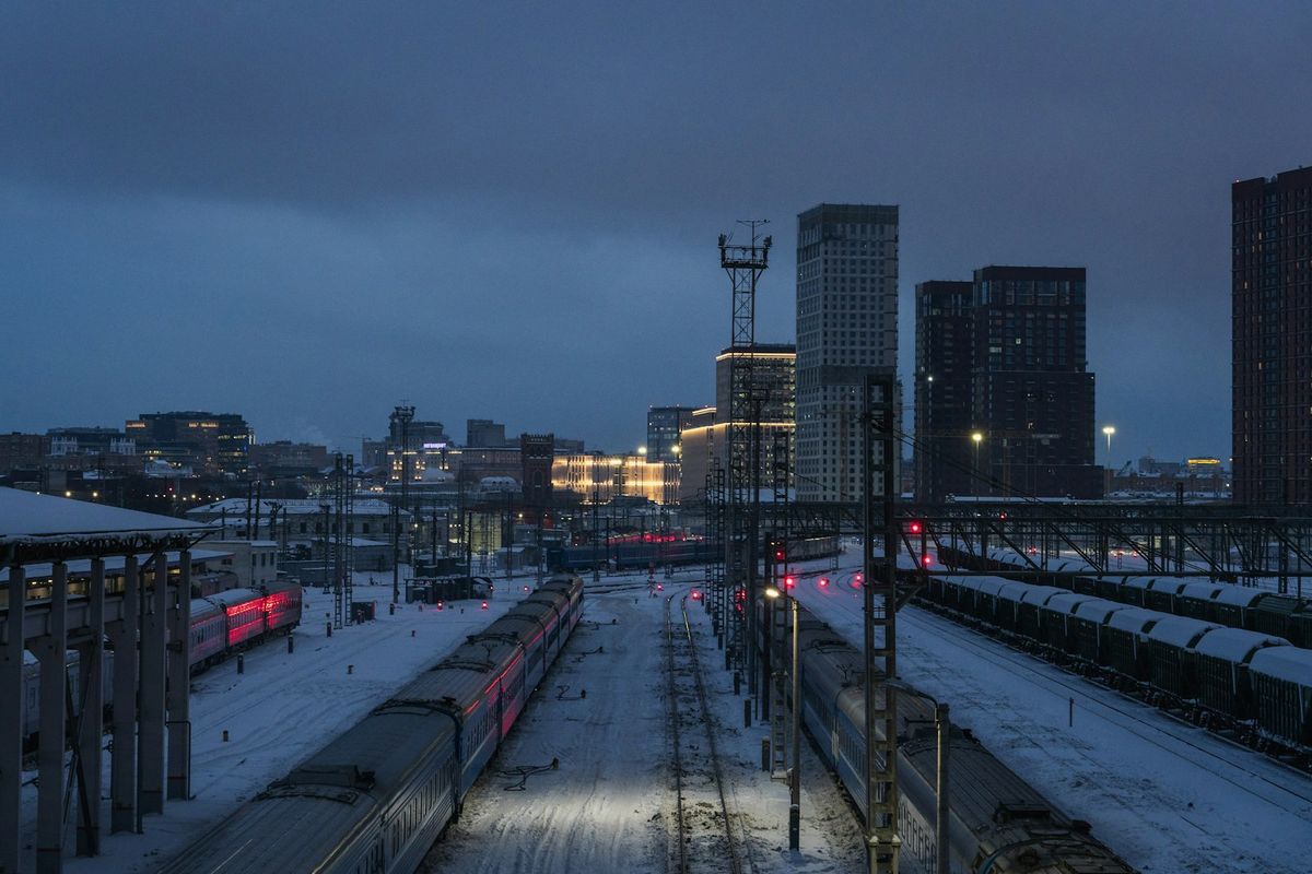 Trains at a snowy station with city buildings at dusk