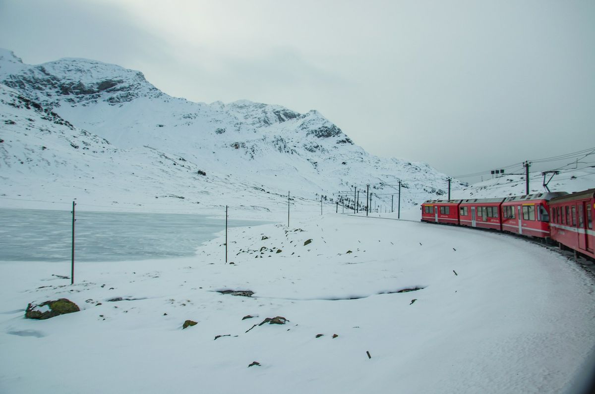 Red train travelling past a snow-covered mountain in Scandinavia