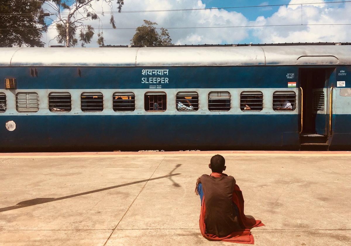 Passenger sitting beside a blue Indian Railways sleeper coach