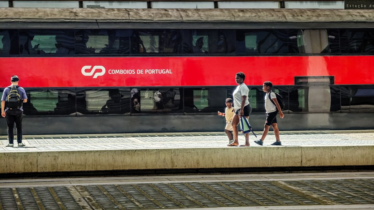 Passengers on a platform next to a red Portuguese train