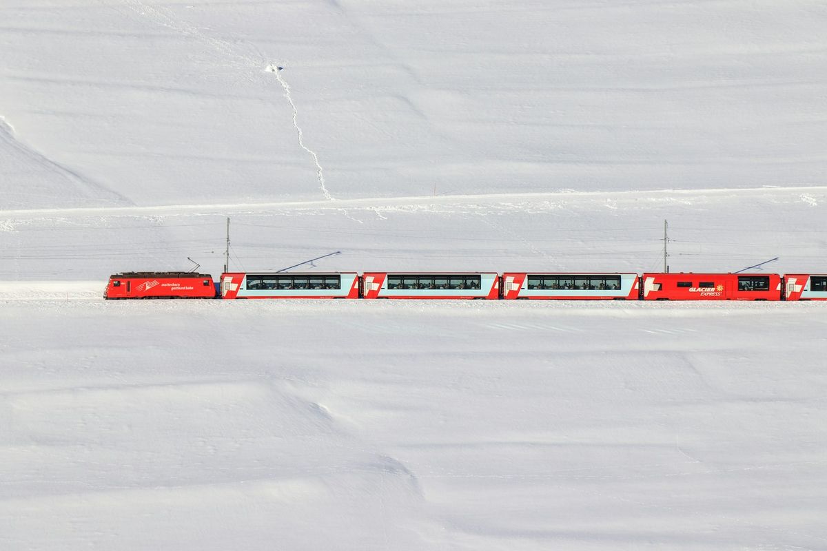 The Glacier Express red train traveling through a snow-covered Swiss landscape