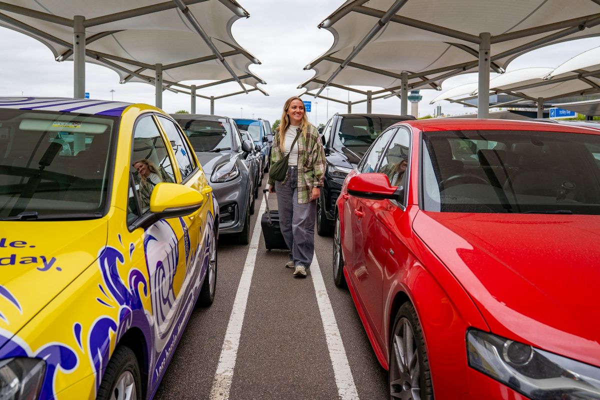 Woman with a suitcase walking between parked rental cars