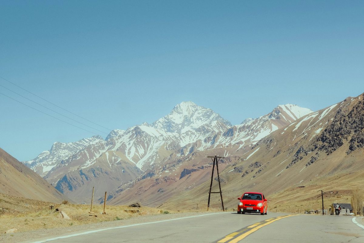 Red car driving on road towards snowy mountains at a border