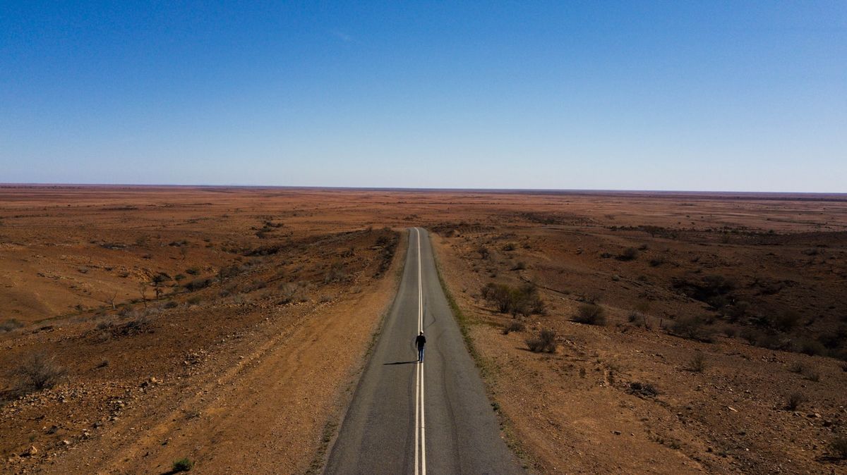 Straight road through brown outback landscape under blue sky in Australia