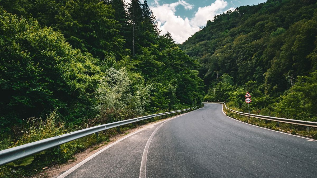 Gray concrete road between green trees under blue sky in Bulgaria