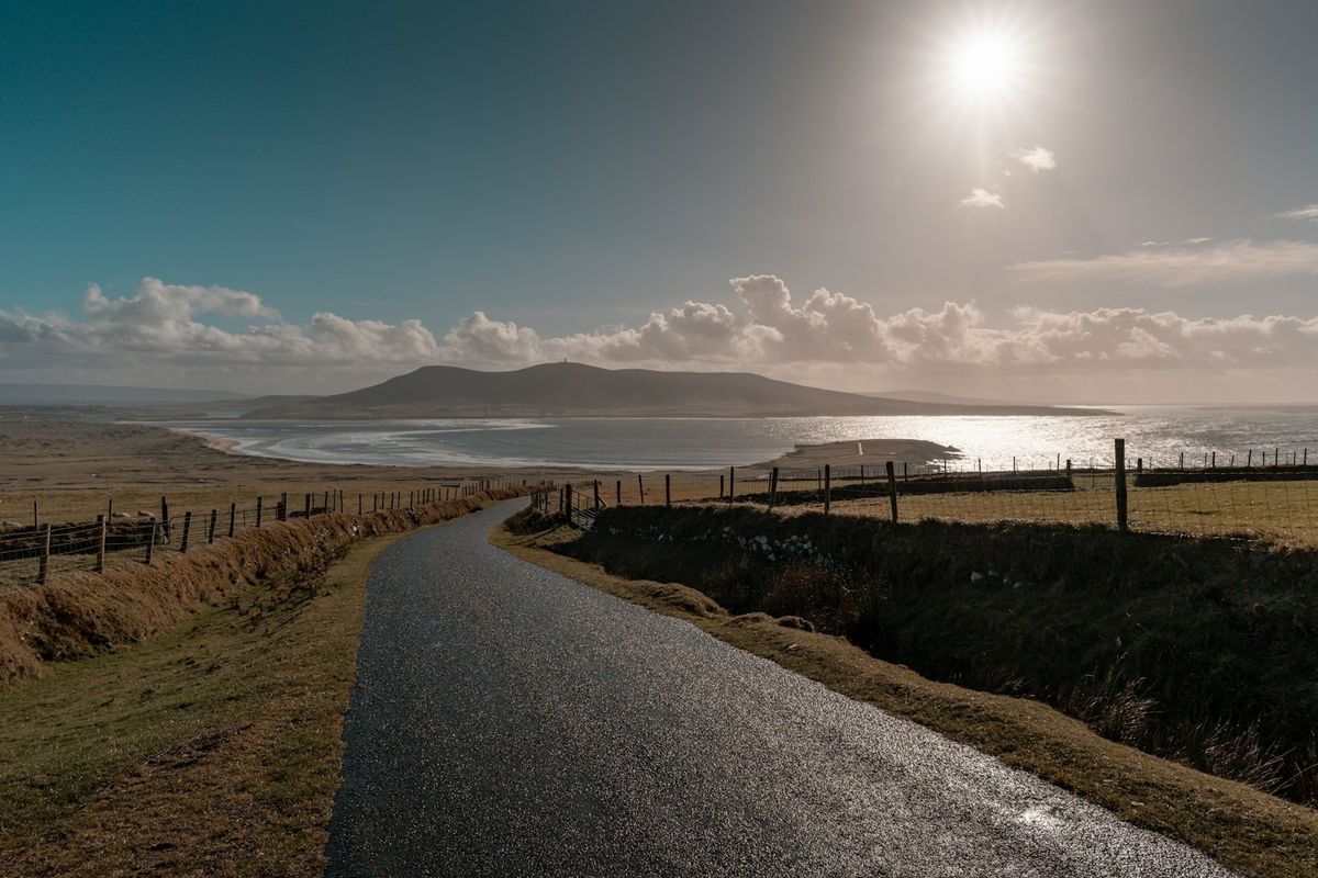 A winding road leading to an Irish coastal landscape under sunlight