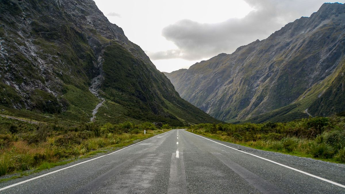 Paved highway winding through a lush mountain valley in New Zealand
