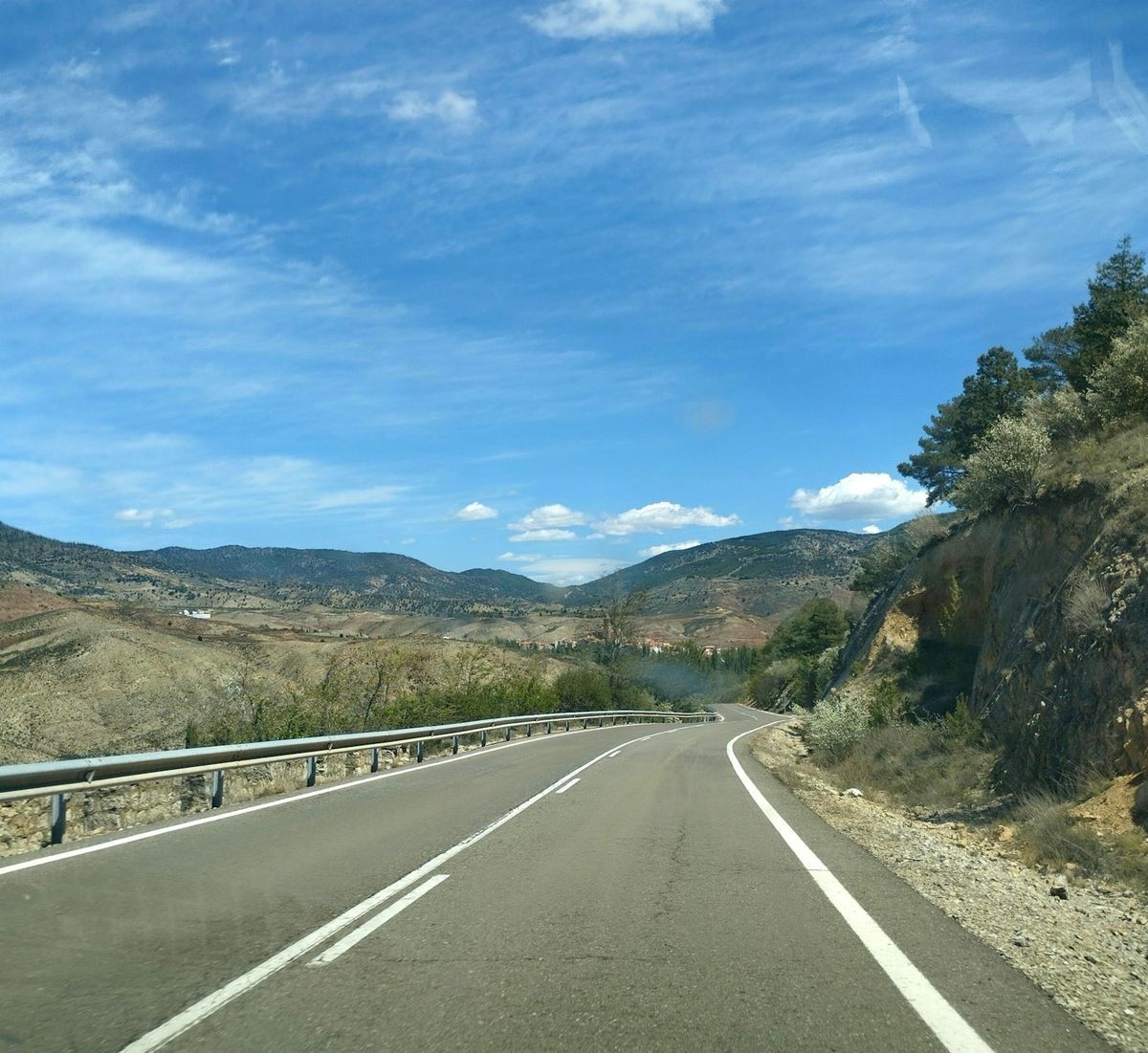 A winding road through rolling Spanish hills under a blue sky