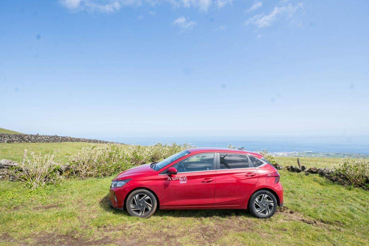 Red rental car parked on a grassy hill overlooking the coast