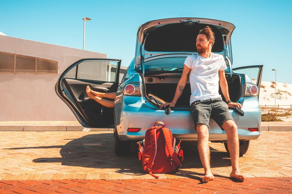 Traveler sitting on the rear bumper of a rental car