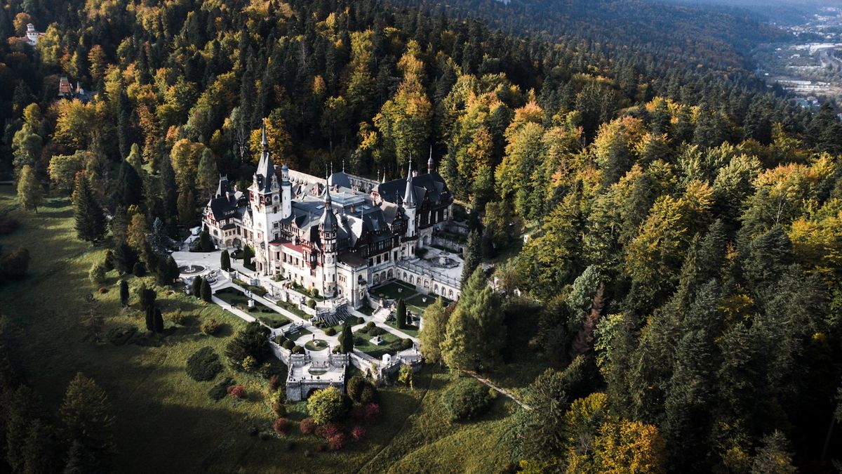Aerial view of Peles Castle surrounded by forest canopy, Sinaia, Romania