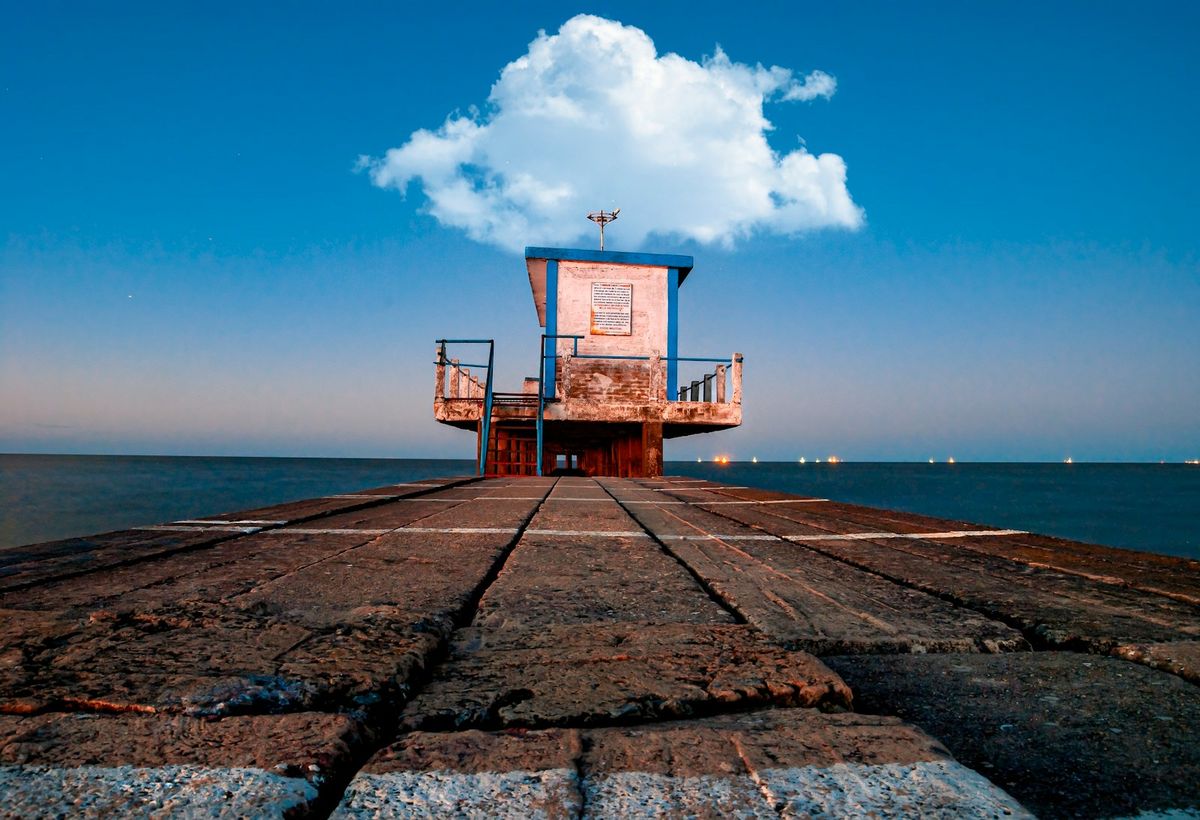 A weathered pier and lighthouse tower reaching into the Rio de la Plata at dusk