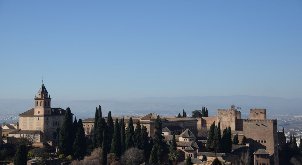 Alhambra palace fortress on hilltop against blue sky, Granada