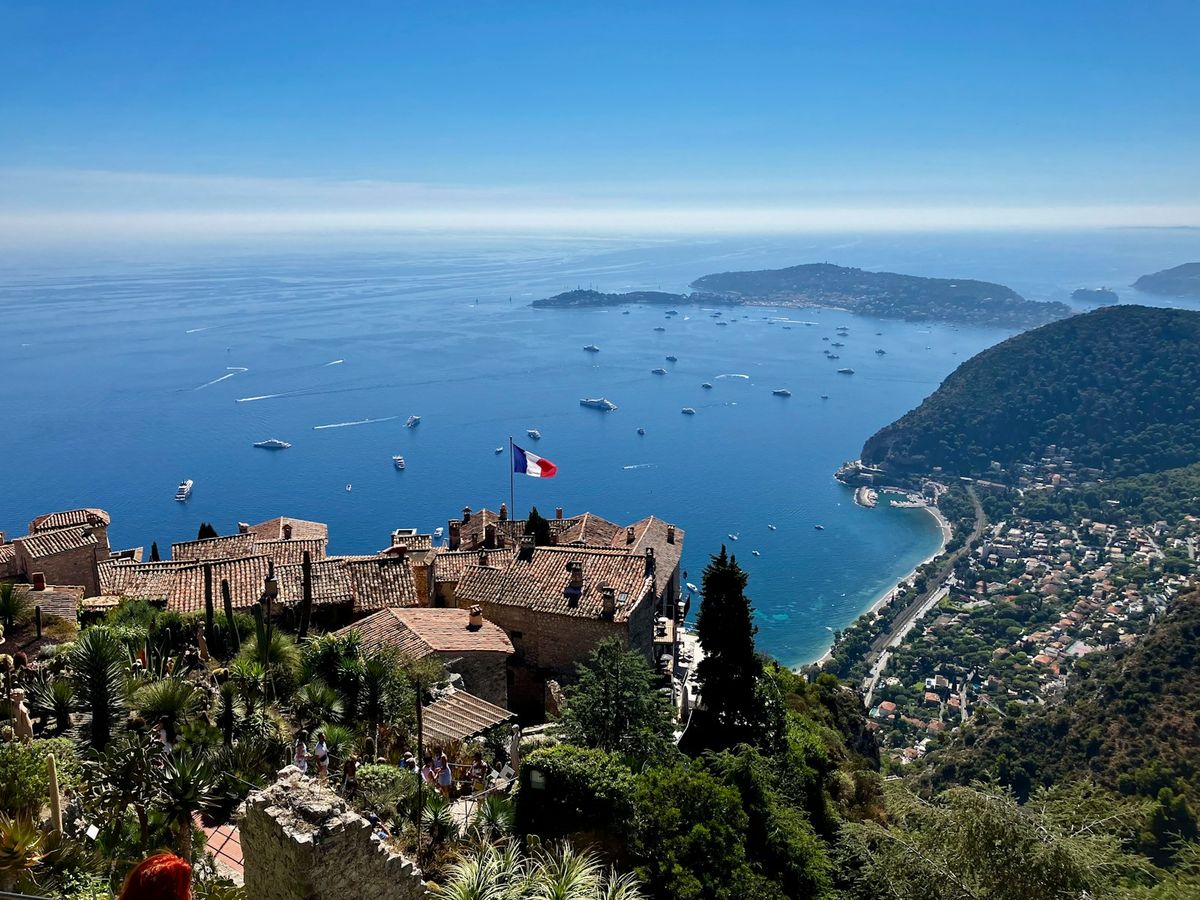 French flag over Eze coastal village with boats in the bay