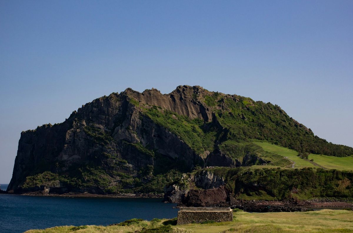Green mountainous volcanic terrain beside coastal waters at Jeju Island