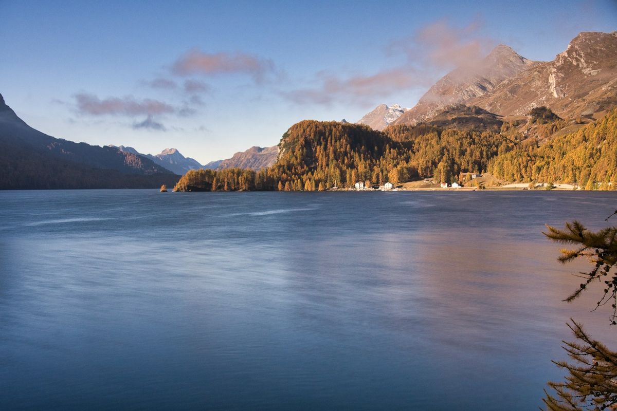 Serene alpine lake with forested mountains in the Engadin valley