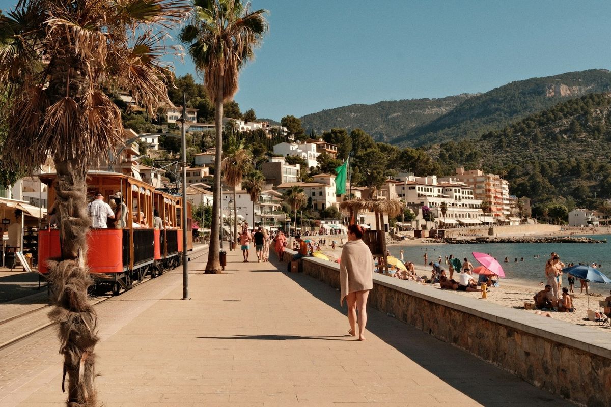 Sunny beach promenade with a train, people, and palm trees