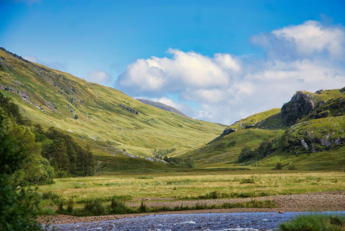 Green Scottish valley with river under clear sky