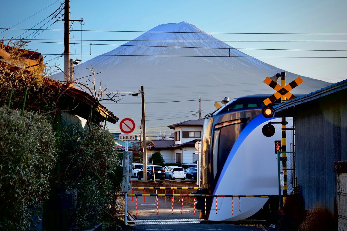 Blue and white bullet train passing a tall snow-capped mountain Japan