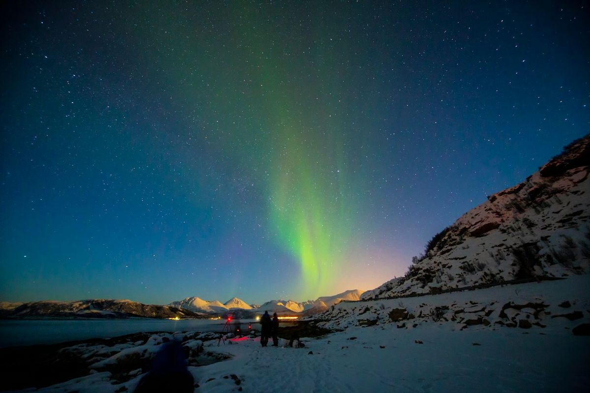 Two people standing under the northern lights at night