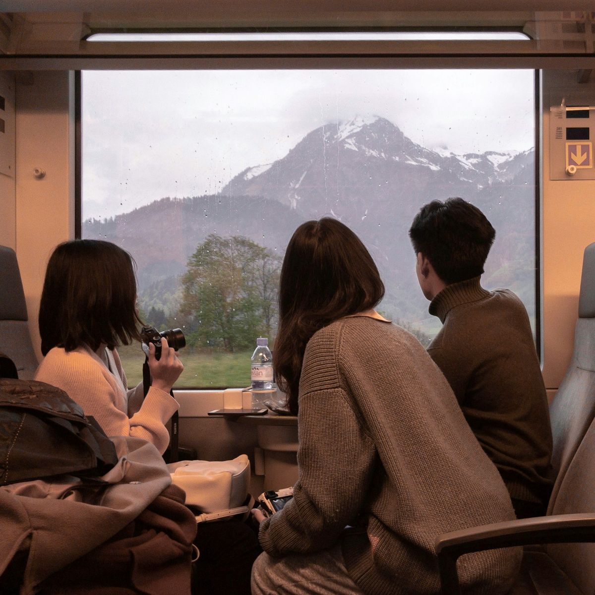 Three people sitting on a train looking out the window at scenery