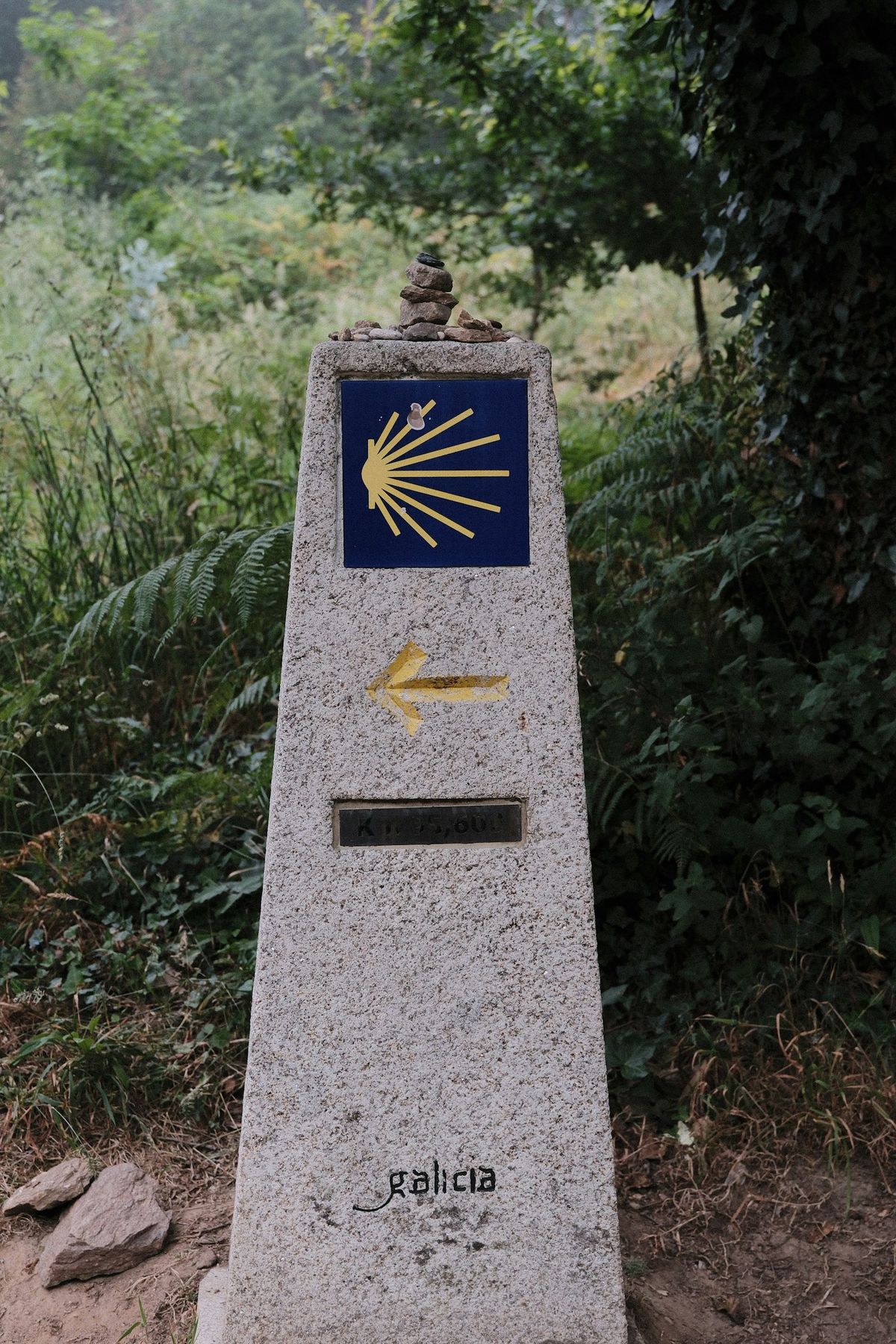 Stone marker with the Camino de Santiago shell and arrow along the trail