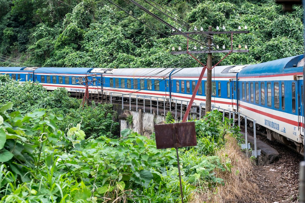 Blue and white train travelling through lush green Vietnamese countryside